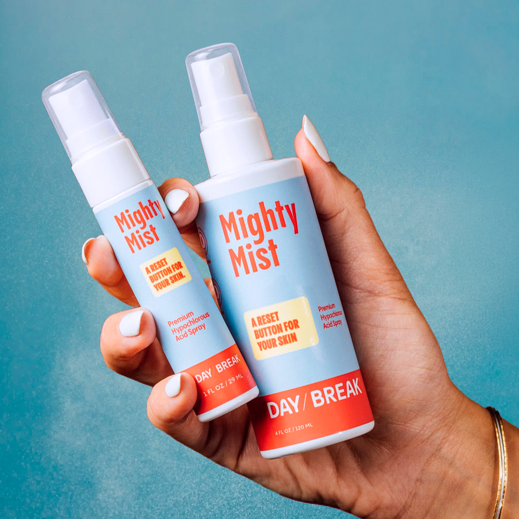Hand holding two 'Mighty Mist' Day Break bottles against a blue background